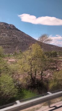 Green farm field rushing past vehicle window, irrigated crop rows with arid hills backdrop, midday sun and rural agriculture vibe,