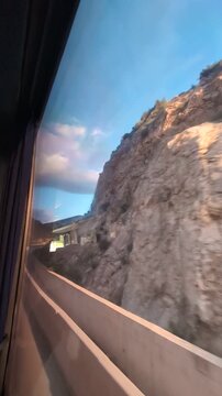 Sunset cliffs rushing past car window, coastal road motion blur, warm golden hour light, speeding travel along rocky shoreline,