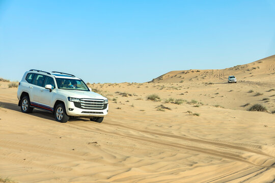 White SUV Driving Across Murqquab Desert Dunes at Sunset, Dubai, United Arab Emirates