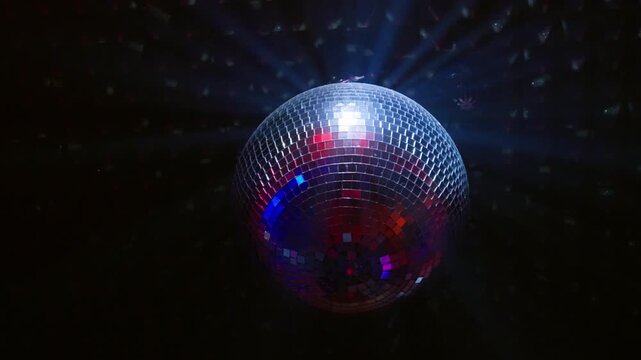 Rotating disco ball with blue and red neon light beams in dark nightclub interior. Vibrant lighting for electronic music rave, techno party, dance event and nightlife entertainment.