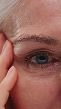 Close-up portrait: old woman face with grey hair, eyes. Concept of plastic surgery of the face, eyelid lift, blepharoplasty, cosmetology. Macro shot of senior female wrinkles near the eyes. Aging skin