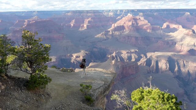 Young female traveler with a backpack reaching a viewpoint at the grand canyon national park, stopping at the cliff edge and triumphantly spreading her arms to embrace the stunning scenery