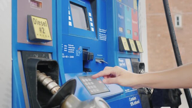 Woman paying for fuel with credit card and entering zip code at blue gas station pump during daytime.