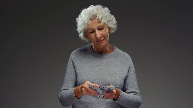 Grandmother counting paper cash. Senior female holding bundle of USD money in hands and throwing one hundred 100 dollar bills. Arms of old woman flipping through currency. Grey hair, wrinkled fingers
