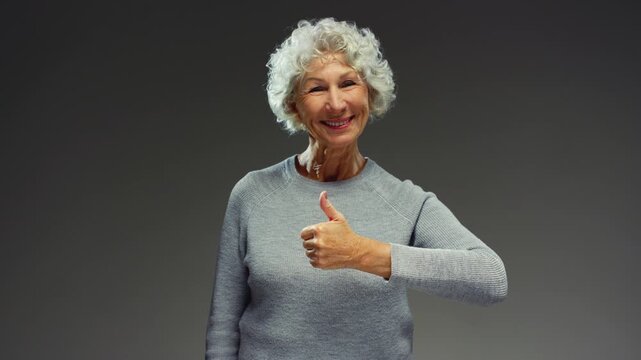 Portrait: elderly female shows the like hand gesture. Old lady, glad senior woman showing, giving thumbs-up hand gesture smiling looking at camera. Face of grandmother, say yes. Grey hair