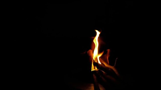 Dramatic close-up of a rustic cup warmed by flickering firelight against a deep black background, evoking warmth