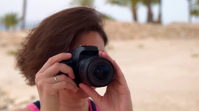 Close up of a focused middle aged woman holding a professional digital DSLR camera and taking photos. Female photographer shooting in a sunny outdoor setting during her travel or creative hobby