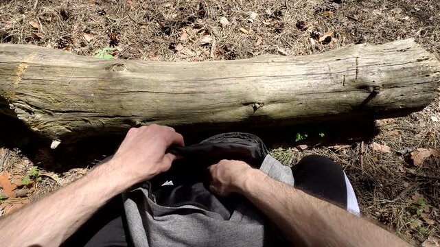 Bushcraft essentials layout POV. A hiker organizes survival tools on a rustic tree trunk: folding knife, LED torch, paracord, and mug