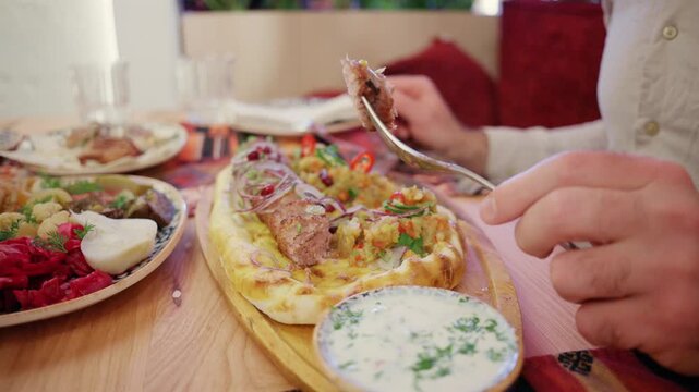 Hands cutting grilled lula kebab on pita bread with knife and fork in restaurant close up view shot.