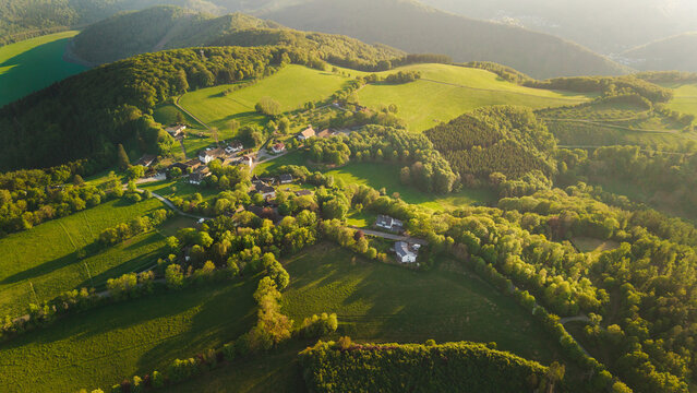Aerial sunset view of peaceful rural village surrounded by green hills forests and farmland in German countryside