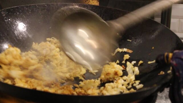Close-up of nasi goreng being stir-fried in a wok, a popular Indonesian fried rice dish in a hot restaurant kitchen.