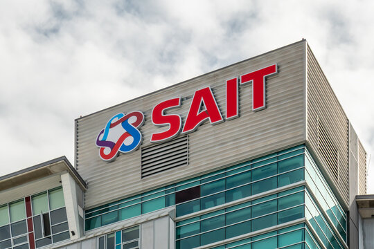 Calgary, Alberta, Canada. May 10, 2026. Exterior low-angle view of the red SAIT logo on a modern glass and steel polytechnic building.