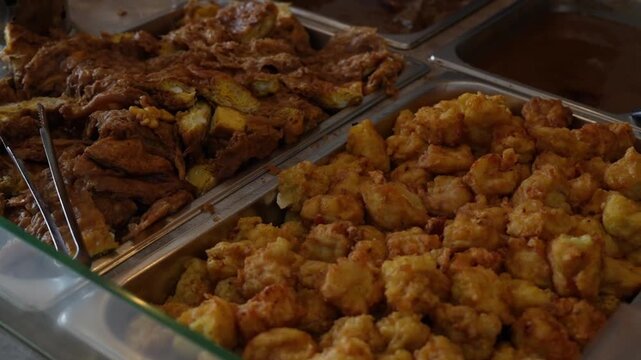 Indonesian fried snacks and tofu displayed in food trays, close-up street food buffet with golden crispy texture