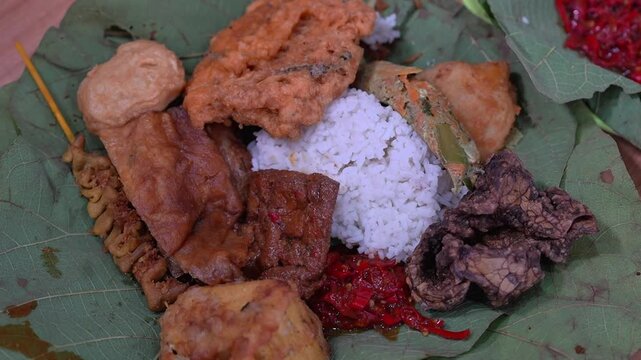 Traditional Indonesian rice meal on teak leaves with sambal, fried tofu, tempeh and assorted side dishes, authentic street food
