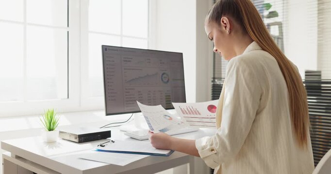 Woman analyst in office reviews computer dashboard. Finance data charts and report guide planning decisions. Bright workspace fosters focused productivity. Clear concept of business analytics.