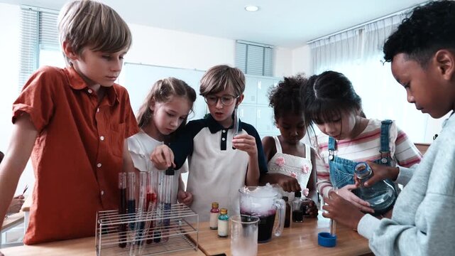 A group of boys and girls of various nationalities stand in front of their classmates learning science, mixing chemicals and holding test tubes in their classroom at school.
