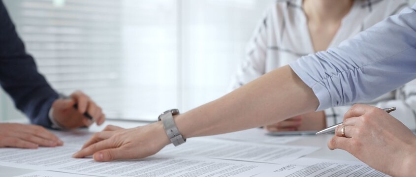 Business people discussing contract documents on a white desk, analyzing clauses and terms during an office meeting, collaborating on important paperwork for agreement