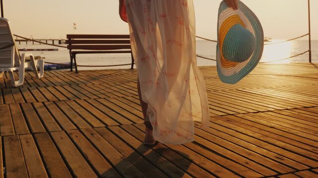 Woman walking on wooden pier at beautiful golden sunset by the sea.