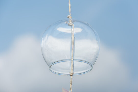Traditional Japanese glass wind chime hanging against a beautiful blue sky with white clouds. A refreshing and minimalist summer scene with copy space, perfect for seasonal greetings, web banners, and