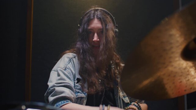 Young female drummer passionately playing a drum kit in a professional rehearsal studio, energetically striking cymbals and drums with drumsticks. Hair flying. Rock Feminist style. Woman power.