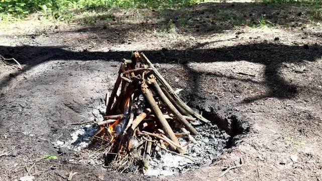 Bushcraft and wilderness survival concept. Cinematic shot from a tripod showing a person successfully lighting a traditional wood fire in spring woods. Camping life and primal skills