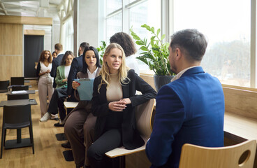 Obraz premium Businesswoman and businessman interview discussion meeting. Two colleagues talk by a window in a bright office as others wait with documents. Concept highlights recruiter candidate communication.