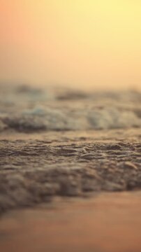 Close-up of gentle sea waves washing onto a sandy beach during golden hour sunset. Beautiful low-angle view with shallow depth of field, Peaceful mood of a summer vacation at the tropical shore.