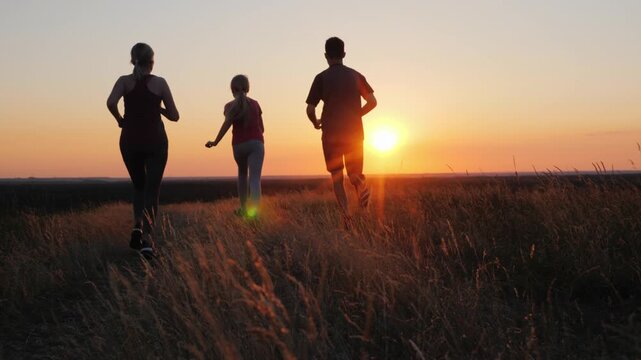 Active family running together across golden grass field during beautiful summer sunset.
