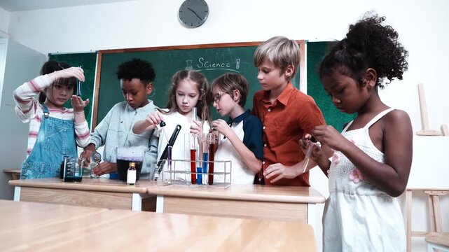 A group of boys and girls, of multinational nationality, stand in front of their classmates learning science, mixing chemicals, holding test tubes in their classroom at school.