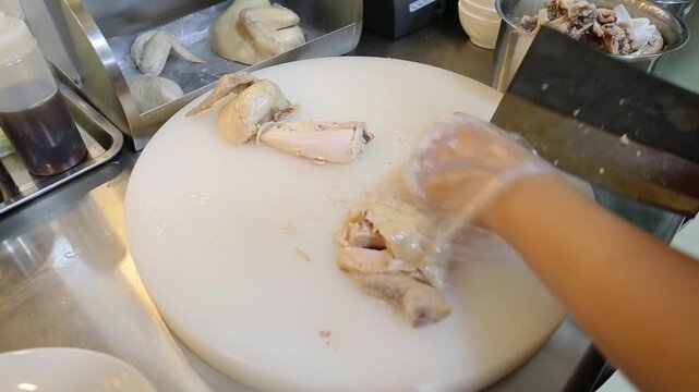 Chef chopping poached chicken with a cleaver on cutting board, close-up Asian restaurant kitchen food preparation