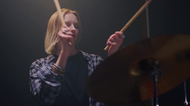 Young female drummer passionately playing a drum kit in a professional rehearsal studio, energetically striking cymbals and drums with drumsticks. Hair flying. Rock Feminist style. Woman power.