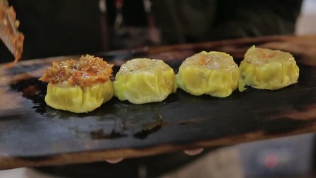 Steamed shumai dumplings topped with sauce, close-up Asian dim sum snack on a hot griddle with warm street food lighting