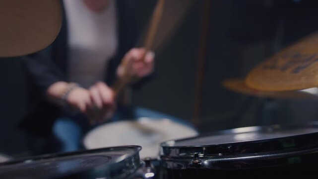 Young female drummer passionately playing a drum kit in a professional rehearsal studio, energetically striking cymbals and drums with drumsticks. Hair flying. Rock Feminist style. Woman power.