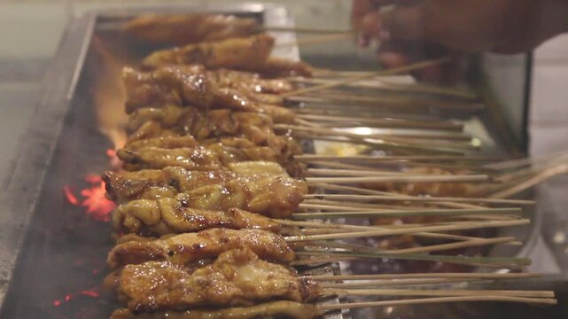 Grilled chicken satay skewers over glowing charcoal, close-up Asian street food barbecue with smoky fire and glossy sauce