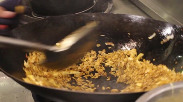 Nasi goreng being stir-fried in a black wok, close-up Indonesian fried rice cooking in a busy restaurant kitchen