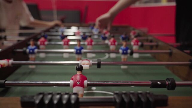 Foosball table with players in red and blue. Hands move sticks with focus and skill. Close-up highlights game intensity and strategy. Perfect for team building or competitive sports scenes