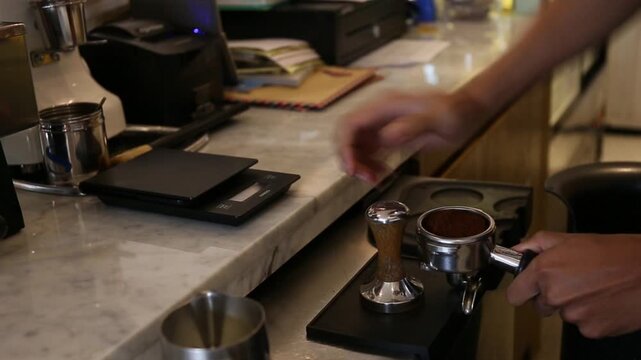 Barista tamping ground coffee in a portafilter, close-up cafe espresso preparation with coffee scale and professional equipment
