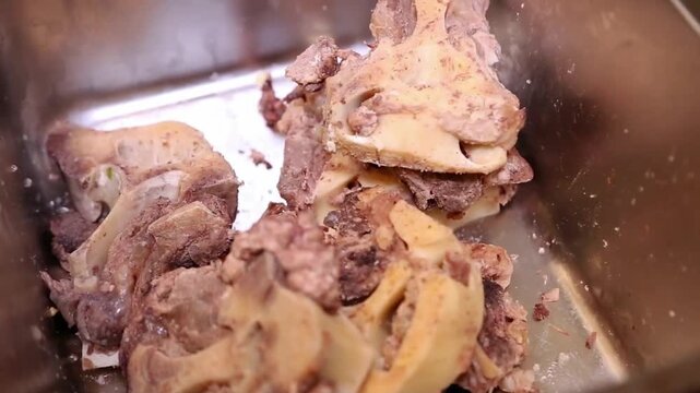 Cooked beef bones and marrow pieces in a metal tray, close-up restaurant kitchen preparation for soup stock and broth