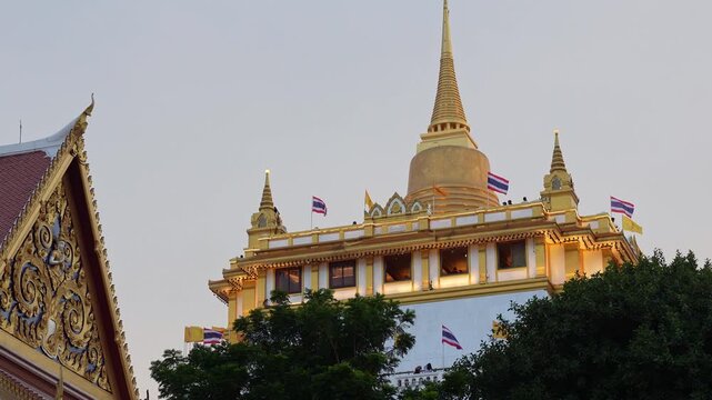 Bangkok, Thailand: Static footage of flags blown by wind in the golden-domed Buddhist stupa of Wat Saket in famous Golden Mount complex of Bangkok, Thailand with the roof of main hall on the side