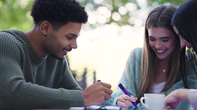 Diverse group of young students smiling and studying together in a park. Happy friends working on a college assignment outdoors on campus