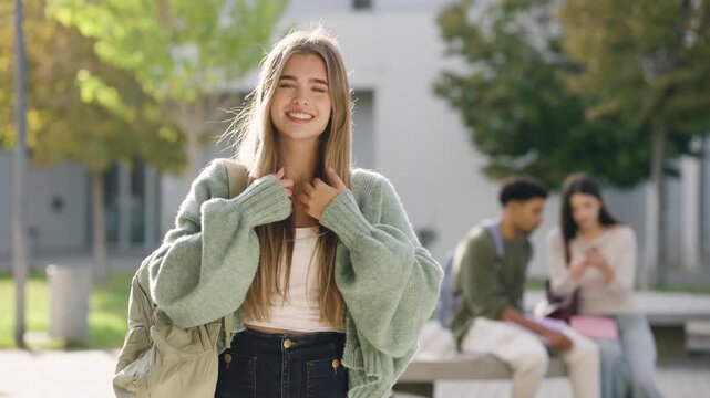 Happy young student with a backpack smiling and posing for the camera at university campus. Multiethnic students talking in the background