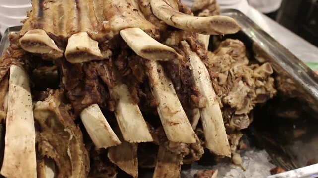 Close-up of cooked beef ribs with large bones on metal tray, roasted meat display in restaurant kitchen with warm lighting