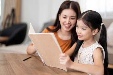 Happy Asian Mother and Daughter Reading a Book Together at Home
