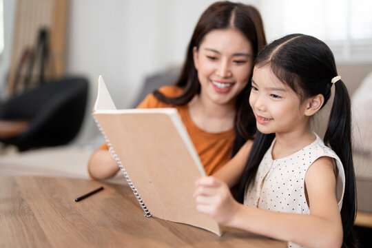 Happy Asian Mother and Daughter Reading a Book Together at Home