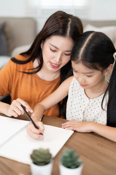 Asian Mother Guiding Daughter with Homework at Home