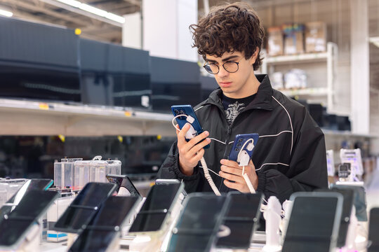 Teenage boy choosing smartphone in electronics store. Technology shopping, consumer decision making, mobile device comparison and digital lifestyle concept.
