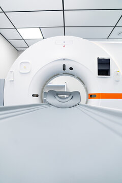 Modern CT scanner machine in bright medical clinic interior. Front view of a white computed tomography scanner with headrest and patient table in a clean hospital room.
