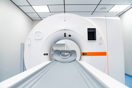 Front view of computed tomography scanner in modern hospital. Symmetrical view of a white CT scanner gantry and patient table in a bright, sterile medical room.