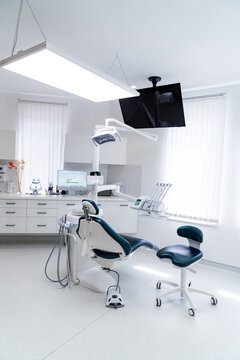 Modern empty dental treatment room with professional medical chair. Interior of a bright clean dental office featuring ergonomic chair, medical equipment, and white cabinet furniture.