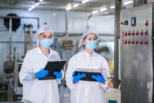 Two individuals in white lab attire, hairnets, and masks. Quality control and hygiene standards in modern canned fish processing factory, concept of food safety and industrial manufacturing.